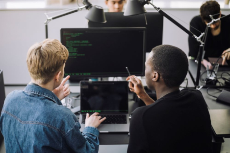 Two developers work together to review code on a monitor.