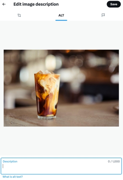 Iced coffee in a glass with milk swirling into the coffee, placed on a countertop in a blurred background